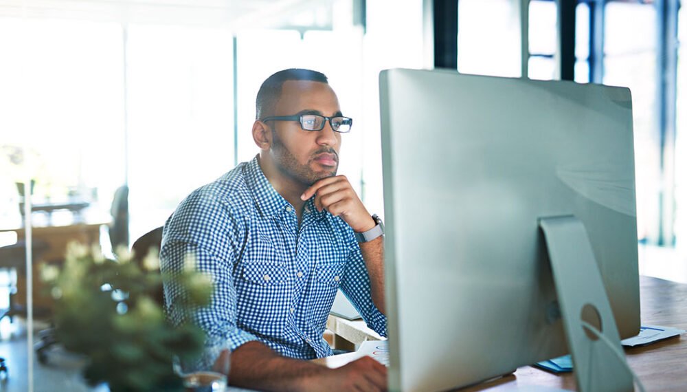 Business man, thinking and computer at desk in office for online research, reading email or report. Male entrepreneur person with internet connection for feedback, review and focus on project.